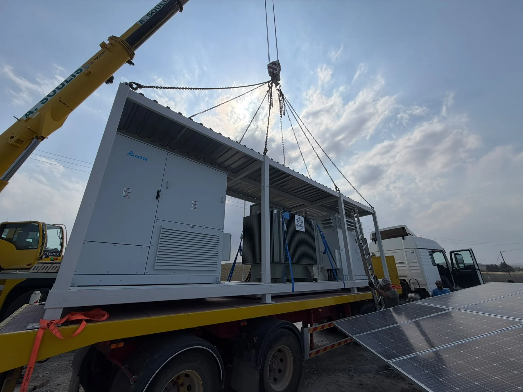 Crane positioning an integrated power conversion and transformer skid beside a solar installation